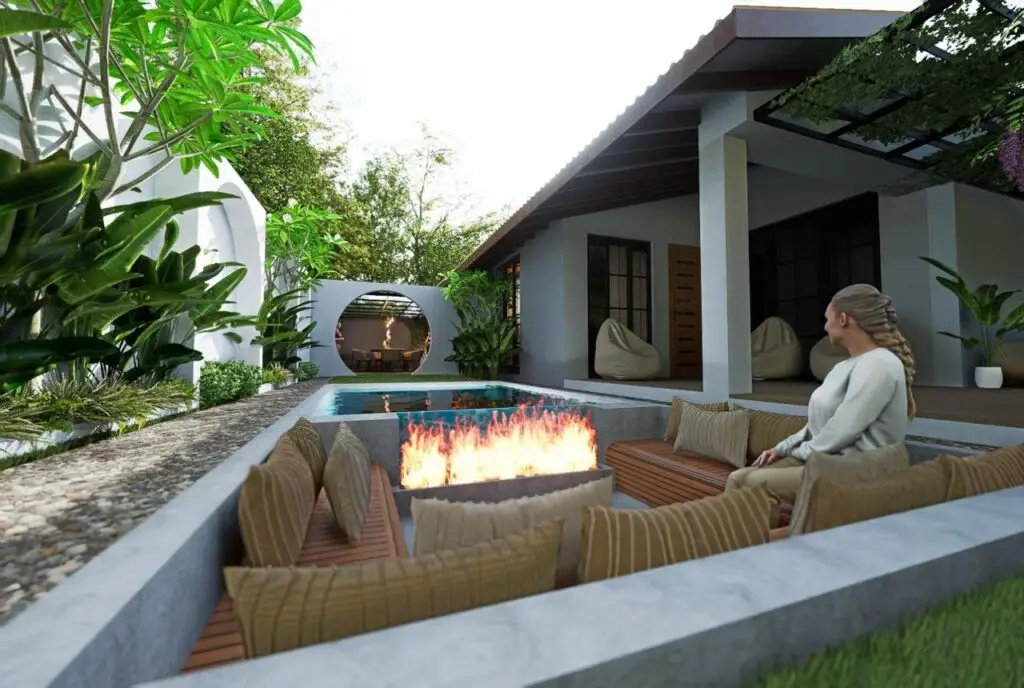 A woman sits by a sunken outdoor fire pit surrounded by cushions, beside a small pool in a modern garden patio, with a contemporary house and lush green plants in the background.renovation