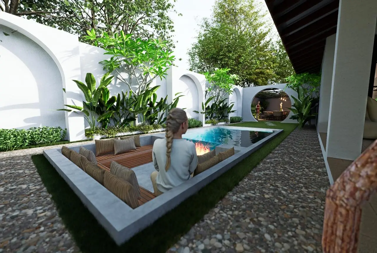 A woman with a braid sits on a sunken outdoor seating area with cushions beside a pool, surrounded by lush greenery, trees, and white arched walls in a modern garden setting.